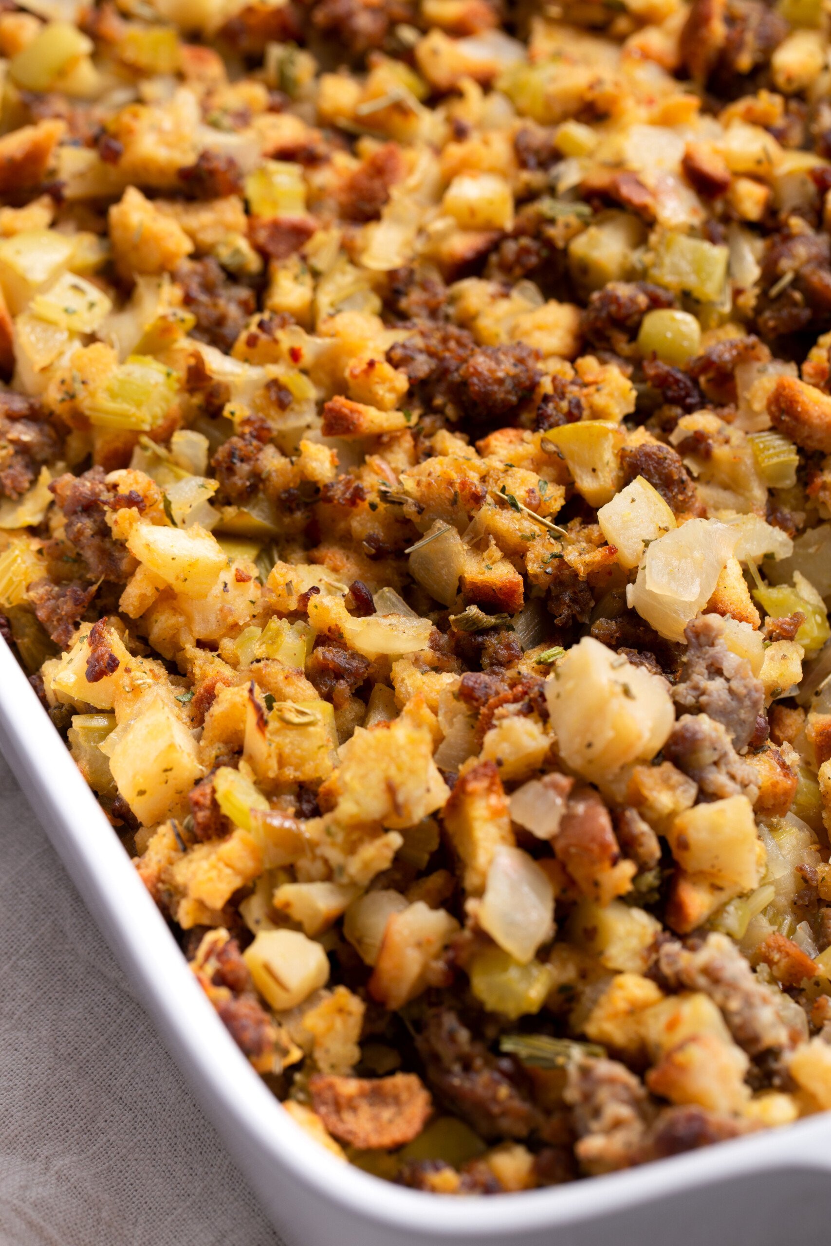 Close up image of sausage and apple stuffing in a white casserole dish.