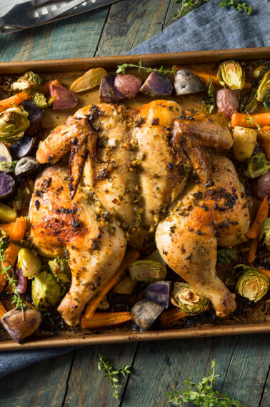 Roasted spatchcock chicken and vegetables on a sheet pan.