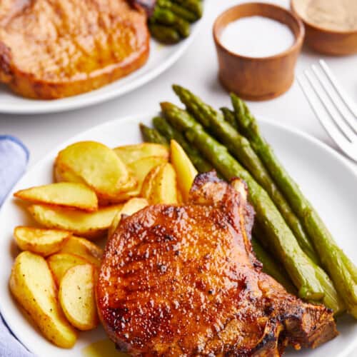 Air fryer bone-in pork chops on a plate with potatoes and asparagus.
