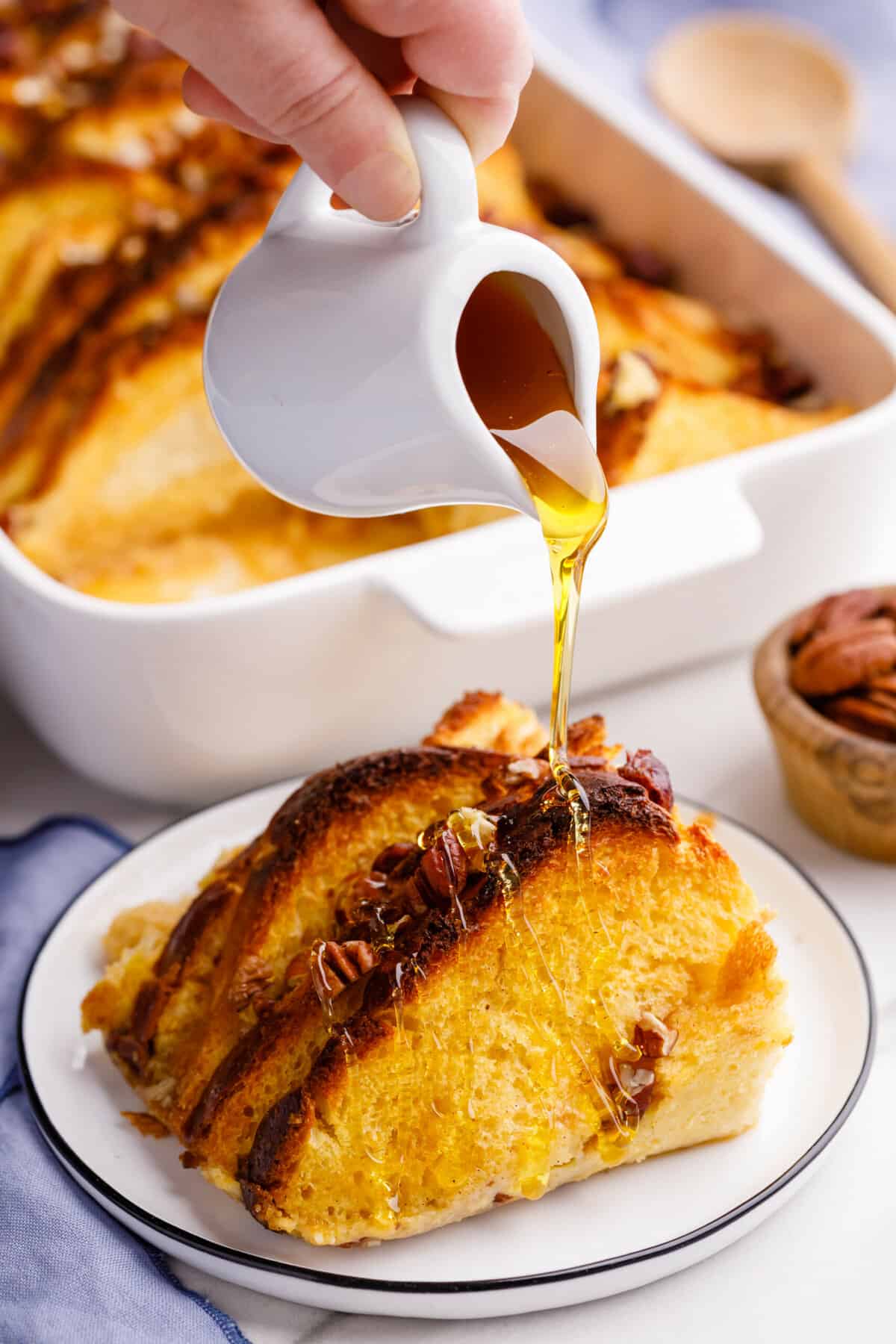 syrup pouring on top of a serving of french toast casserole sitting on a white round plate.