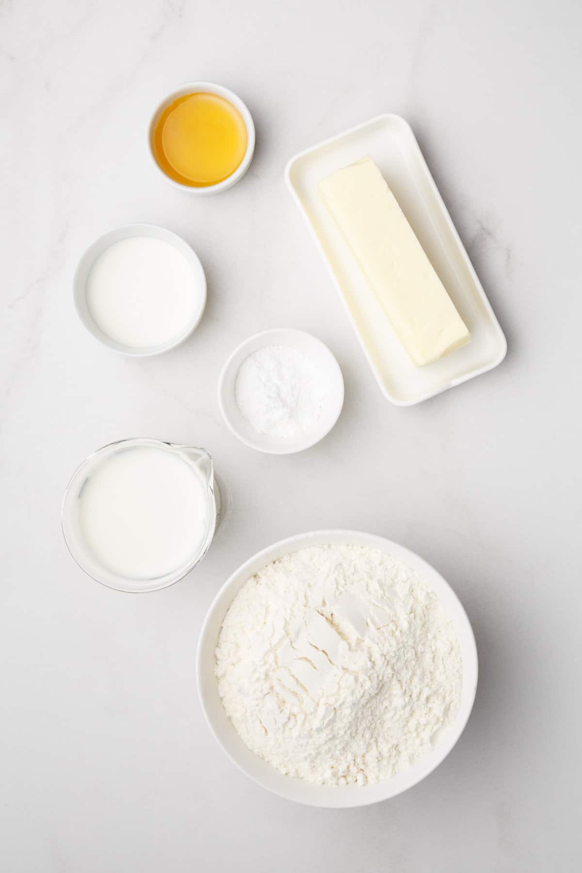The ingredients to make buttermilk biscuits are shown portioned out on a white background.