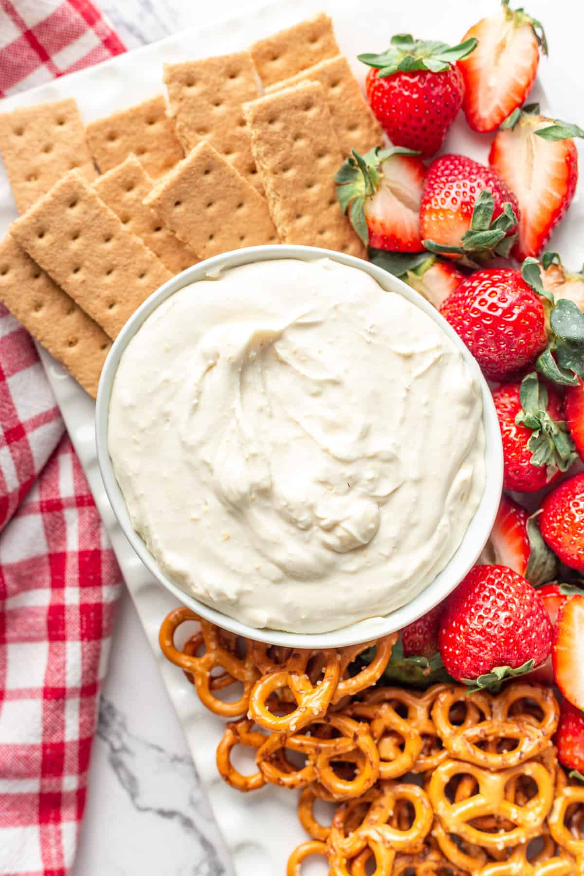 close up image of cheesecake dip served in a white round bowl with a variety of snacks served on the side for dipping