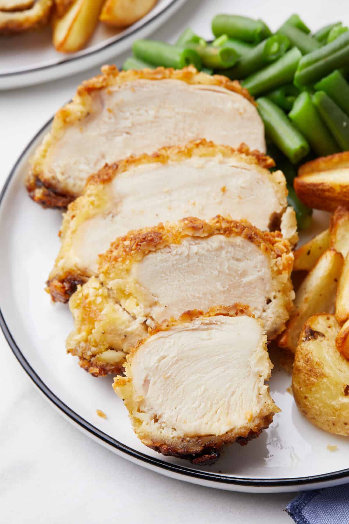 Crispy almond chicken pieces on a plate with potatoes and green beans.