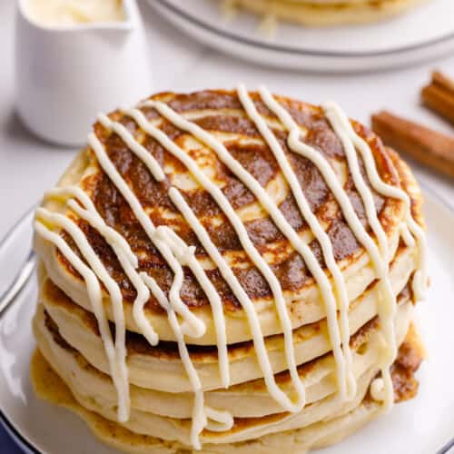 A stack of cinnamon roll pancakes topped with cream cheese frosting.