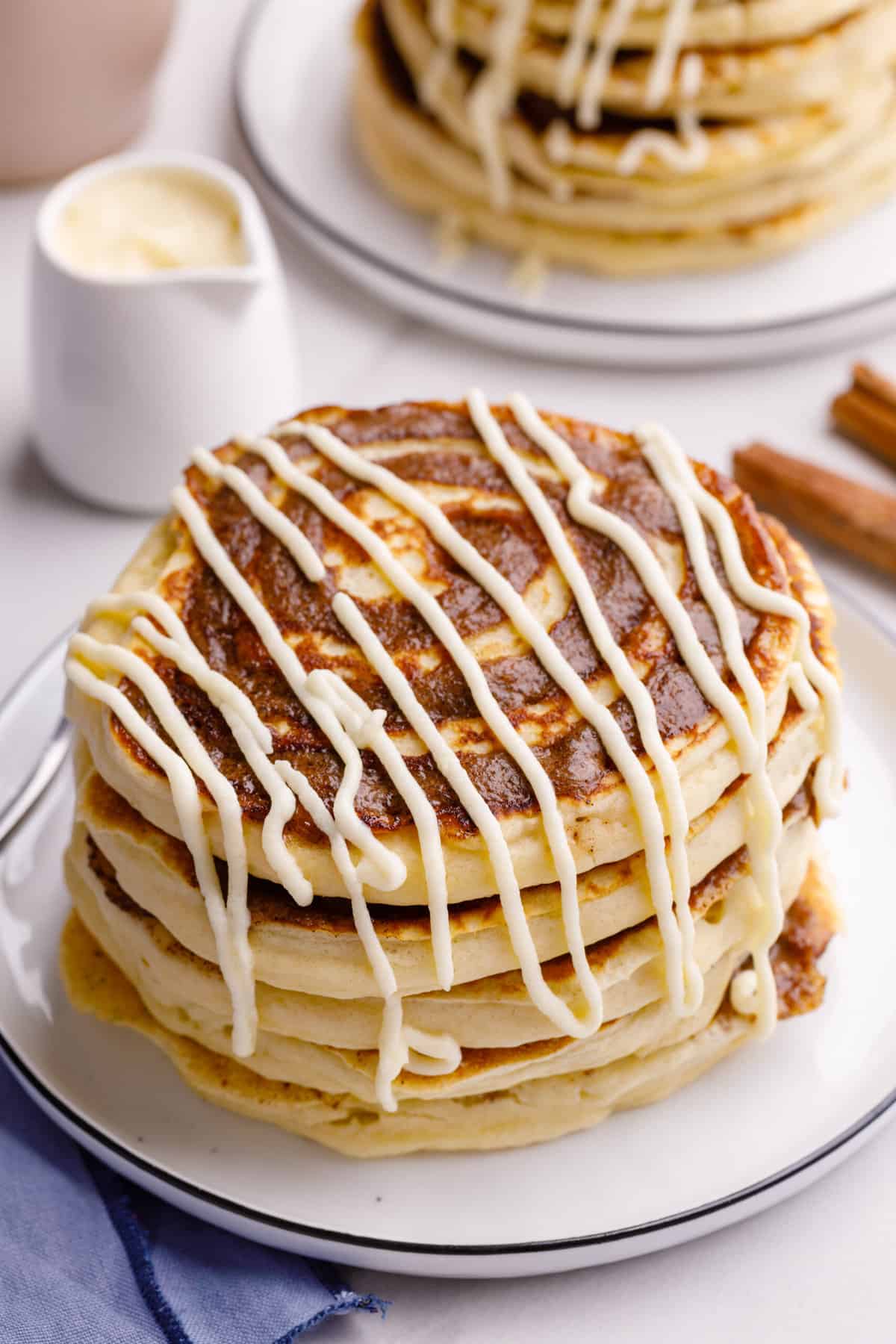 stack of five cinnamon roll pancakes with cream cheese frosting served on a white round plate