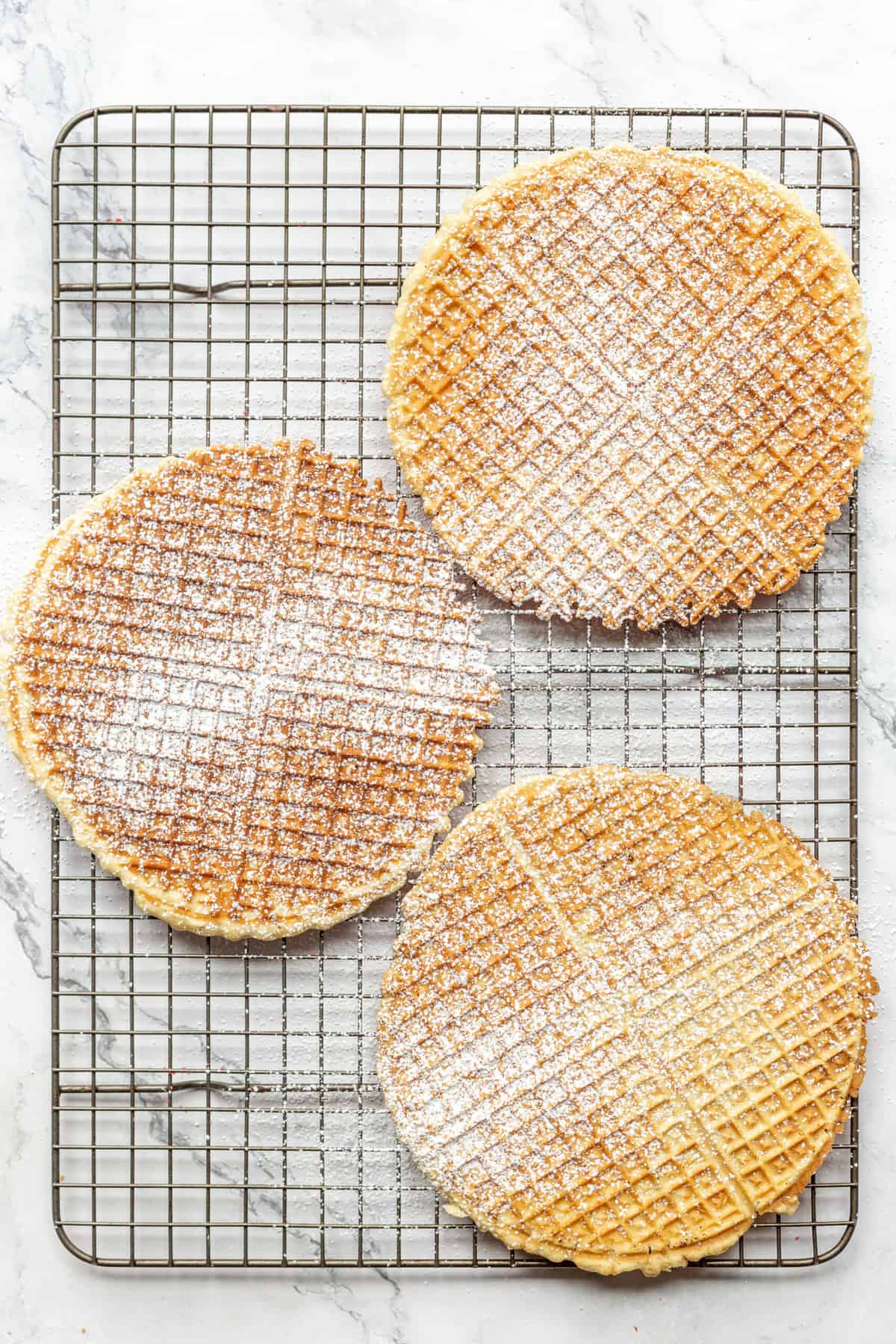 Powdered sugar dusted pizzelle cookies on a wire rack. 