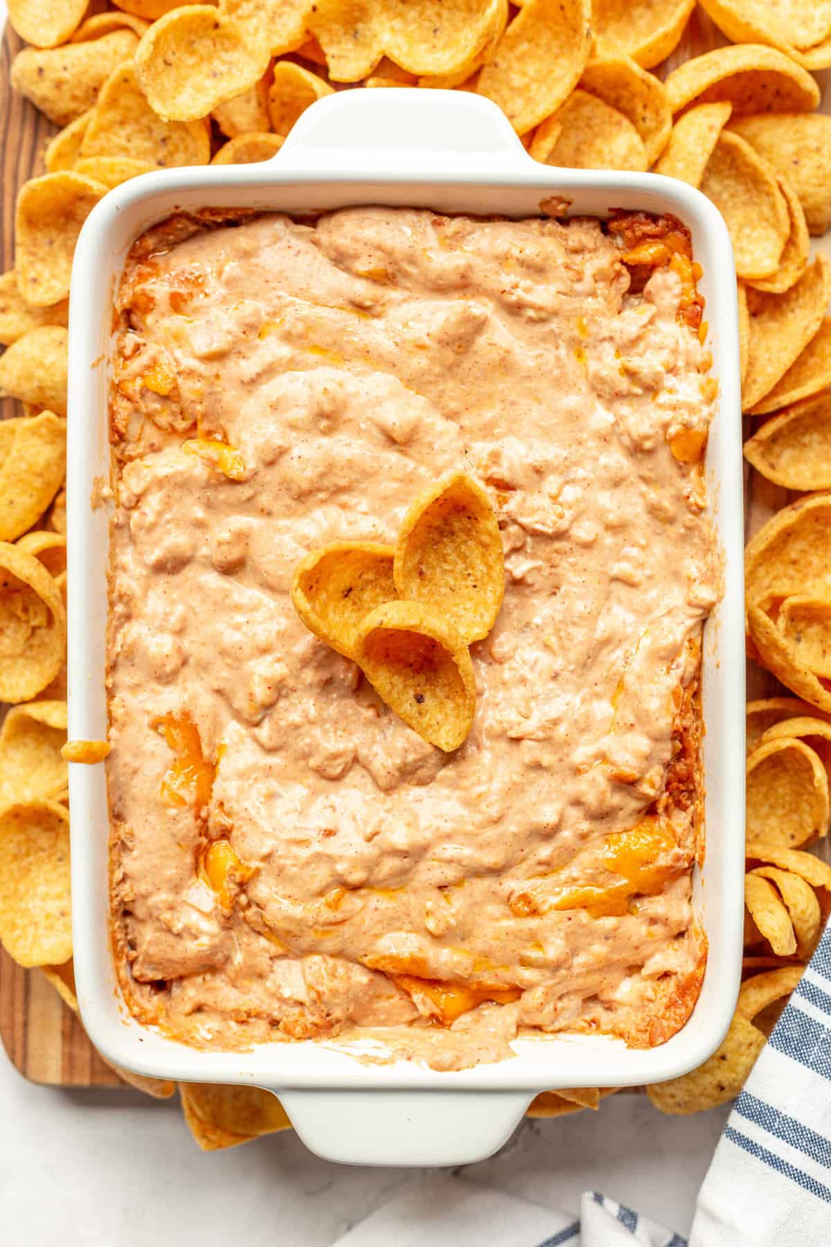 top down image of creamy and cheesy refried bean dip sitting in a large white casserole dish surrounded by frito chips