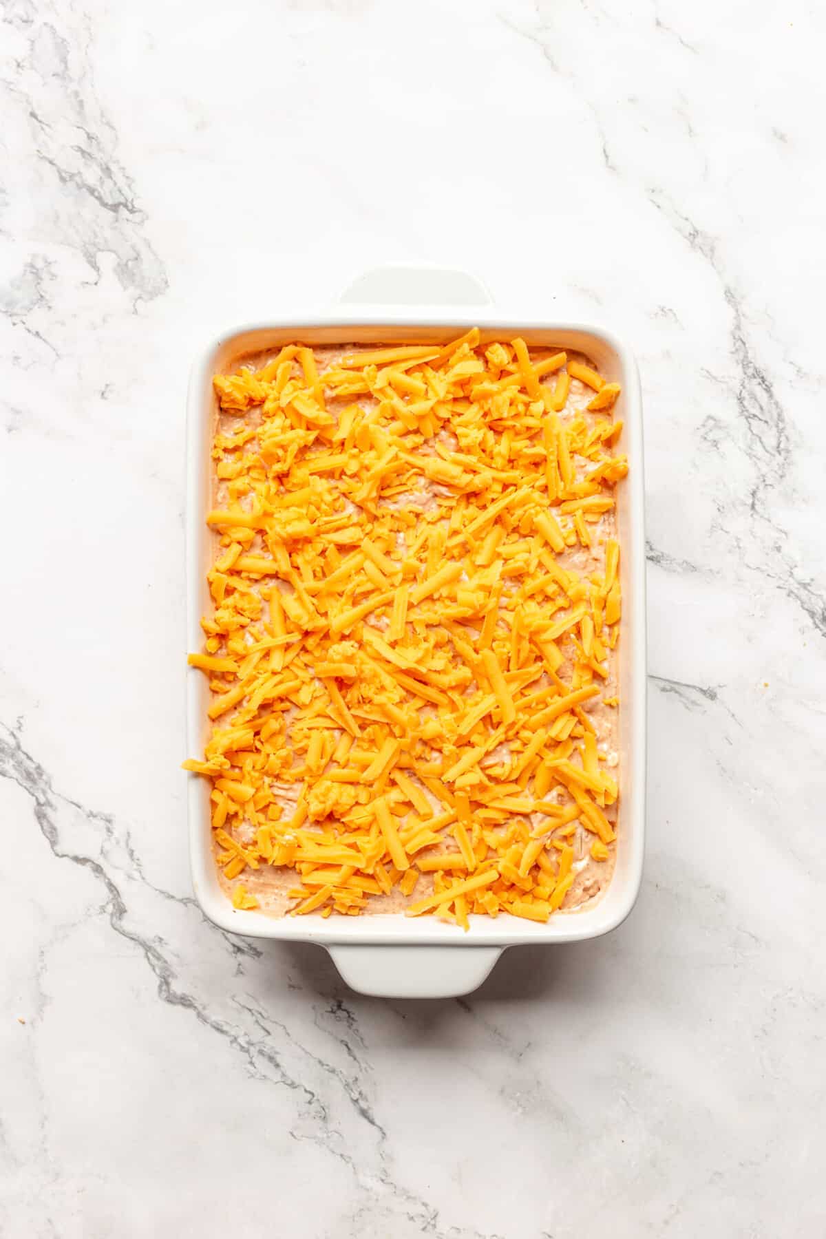 Shredded cheese added to bean dip in dish.
