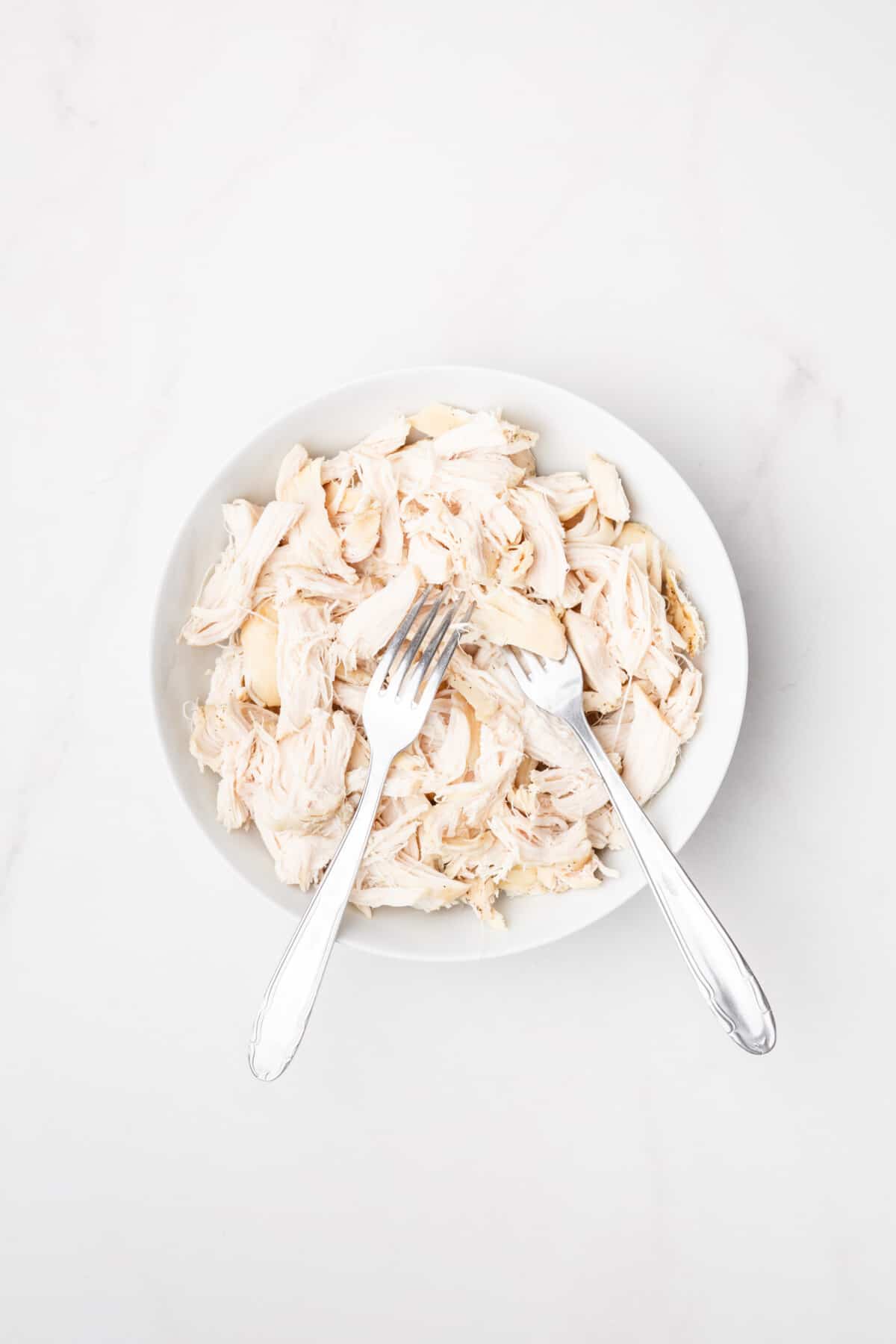 Shredded chicken in bowl with two forks.