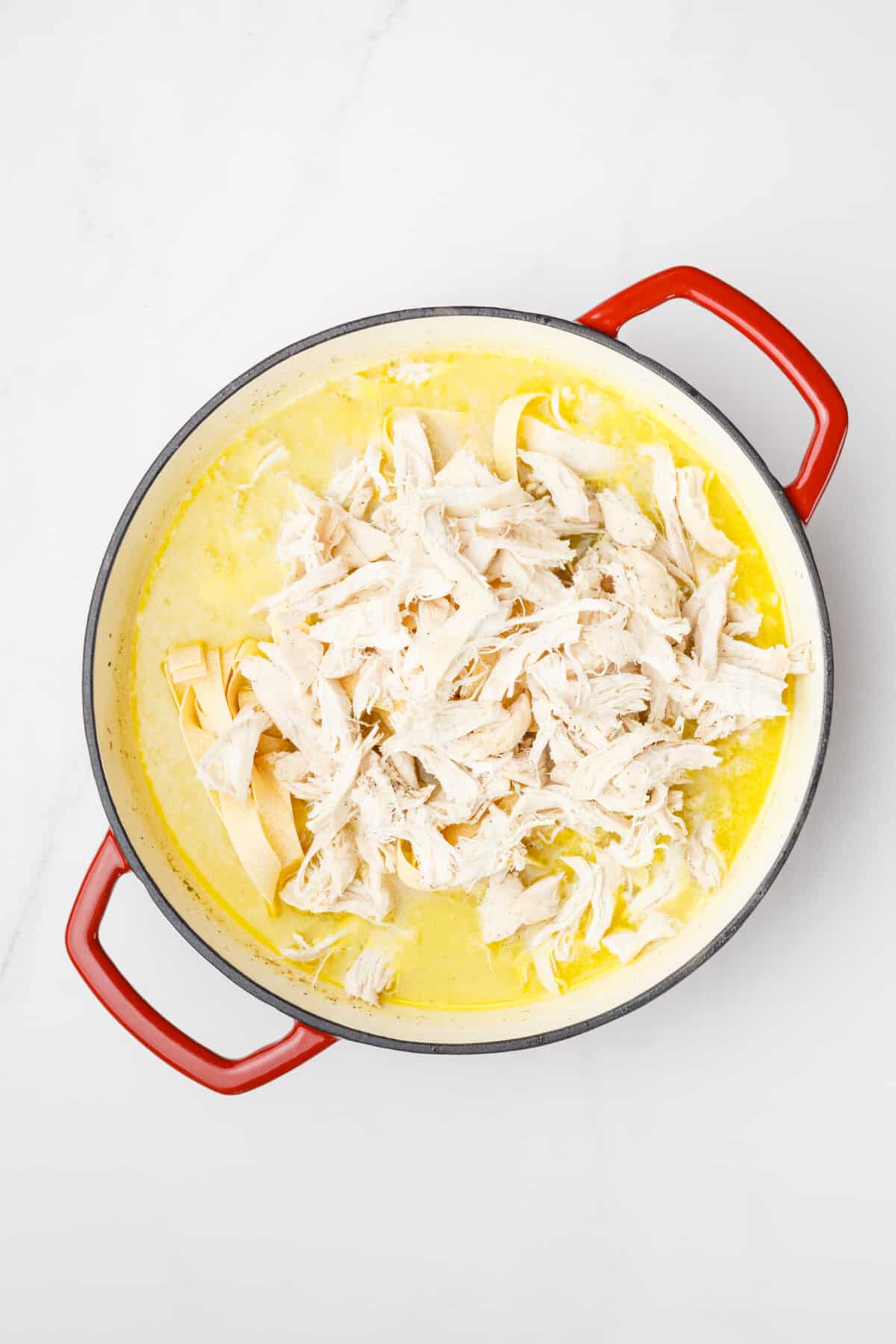 Shredded chicken added to Dutch oven with creamy sauce.