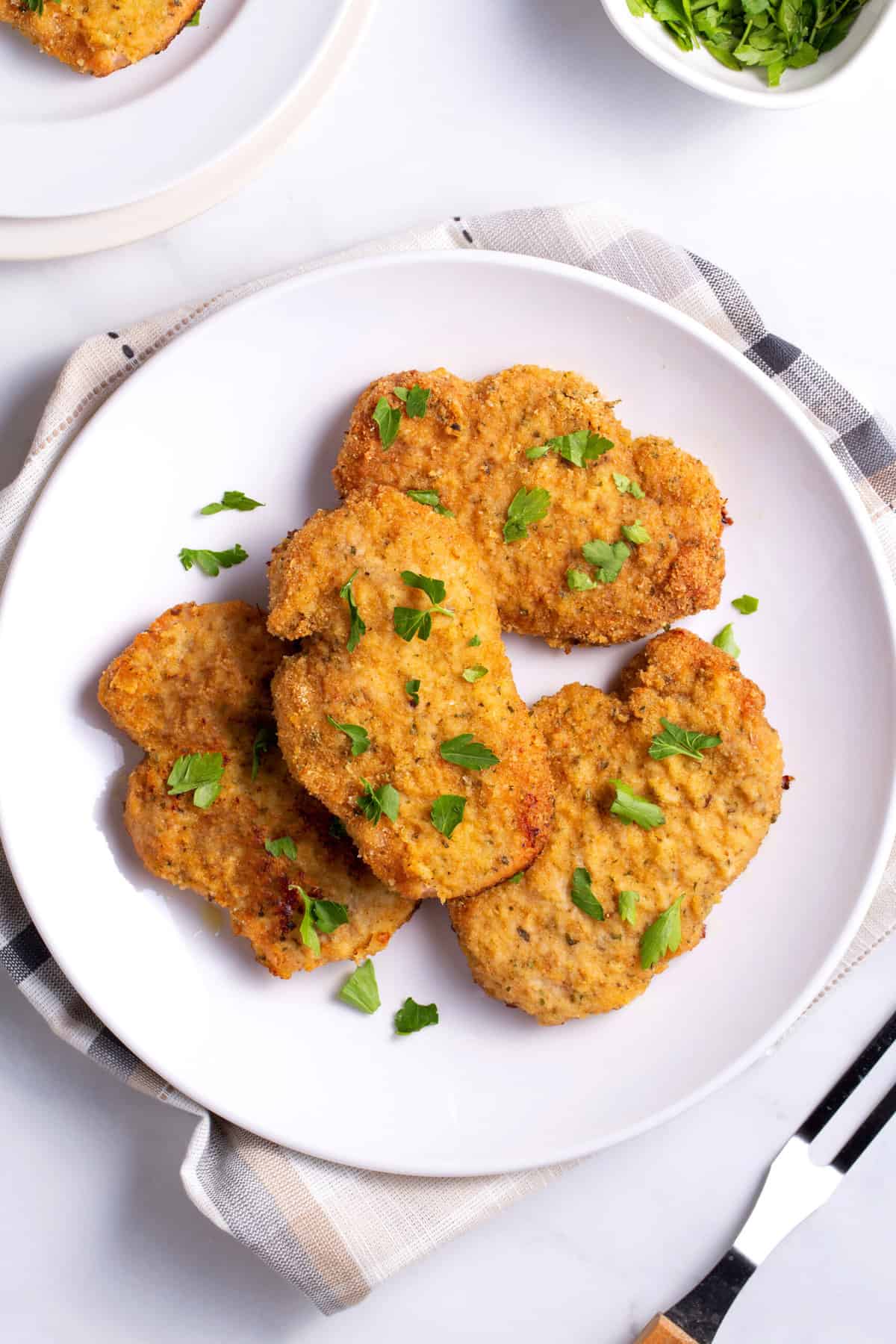 top down image of a plate of baked breaded pork chops served on a white round plate garnished with fresh parsley