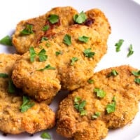 A plate with baked breaded pork chops topped with parsley.