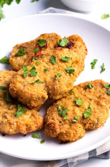 A plate with baked breaded pork chops topped with parsley.