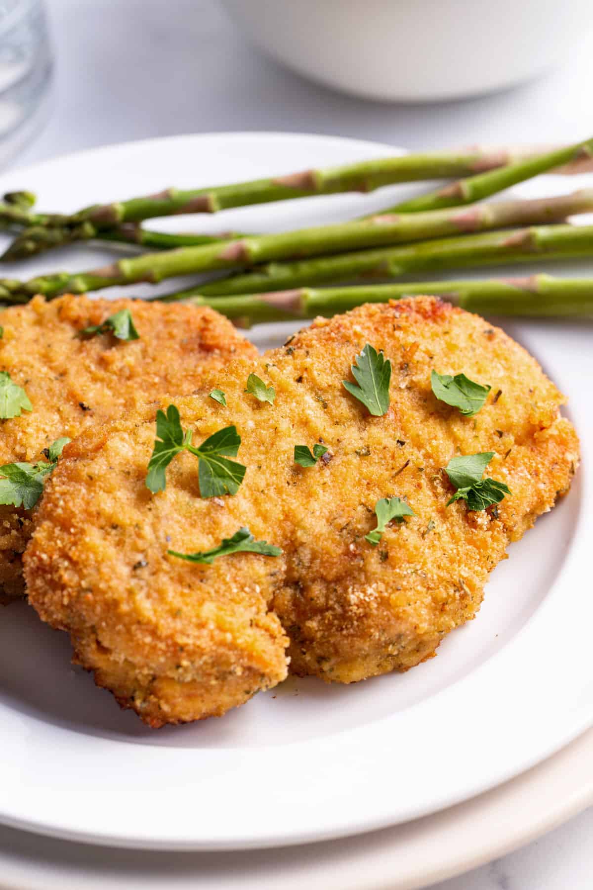 baked breaded pork chops served on a white round plate with a side of asparagus