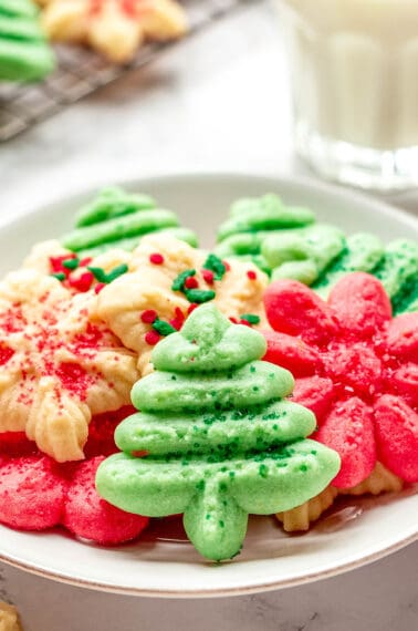A plate of cream cheese spritz cookies in the shapes of Christmas trees, snowflakes, and flowers.