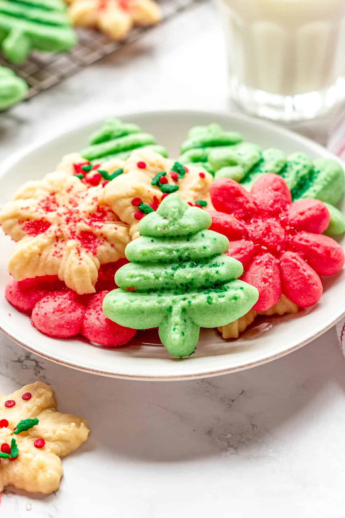 A plate of cream cheese spritz cookies in the shape of Christmas trees, flowers, and snowflakes.