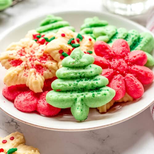 A plate of cream cheese spritz cookies in the shape of Christmas trees, flowers, and snowflakes.