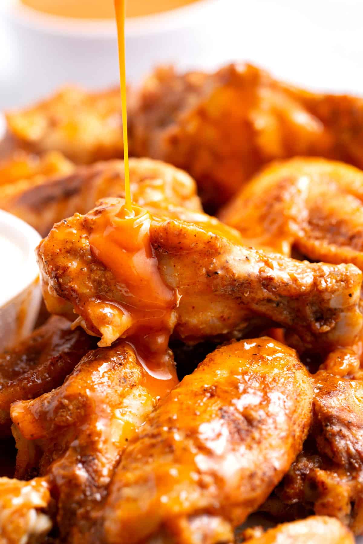 buffalo sauce being poured on a pile of crockpot chicken wings