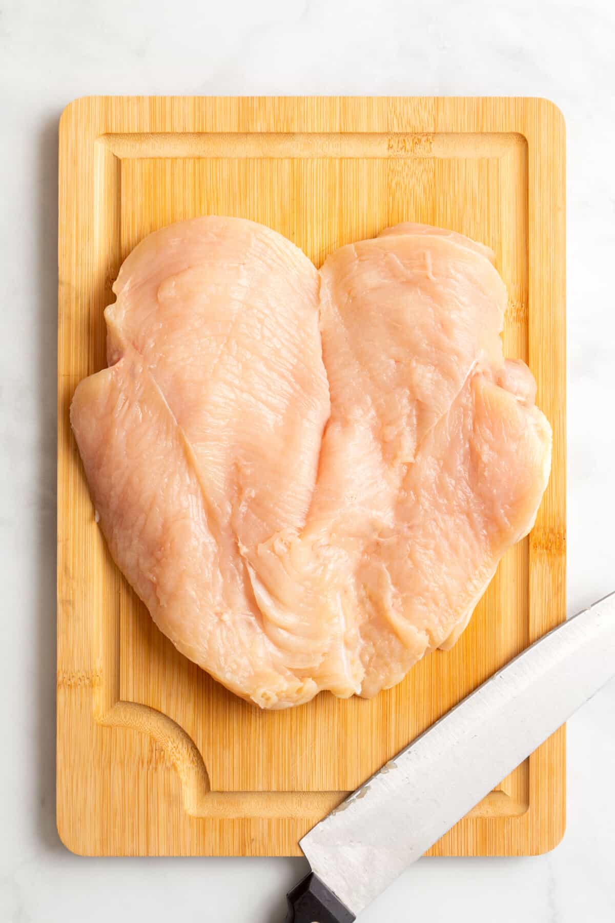 A raw butterflied chicken breast on a wooden cutting board. 