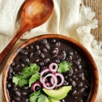 A bowl of black beans topped with red onion, cilantro, and avocado.