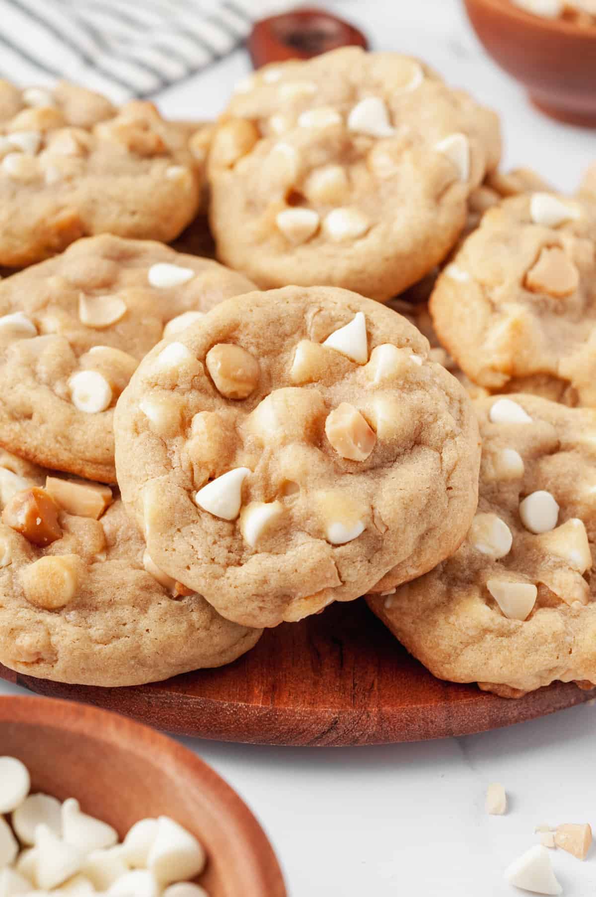 close up image of a pile of macadamia nut cookies served on a round wooden board