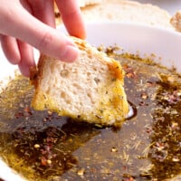 A piece of bread being dipped into olive oil bread dip.