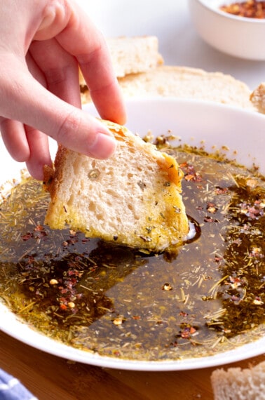 A piece of bread being dipped into olive oil bread dip.