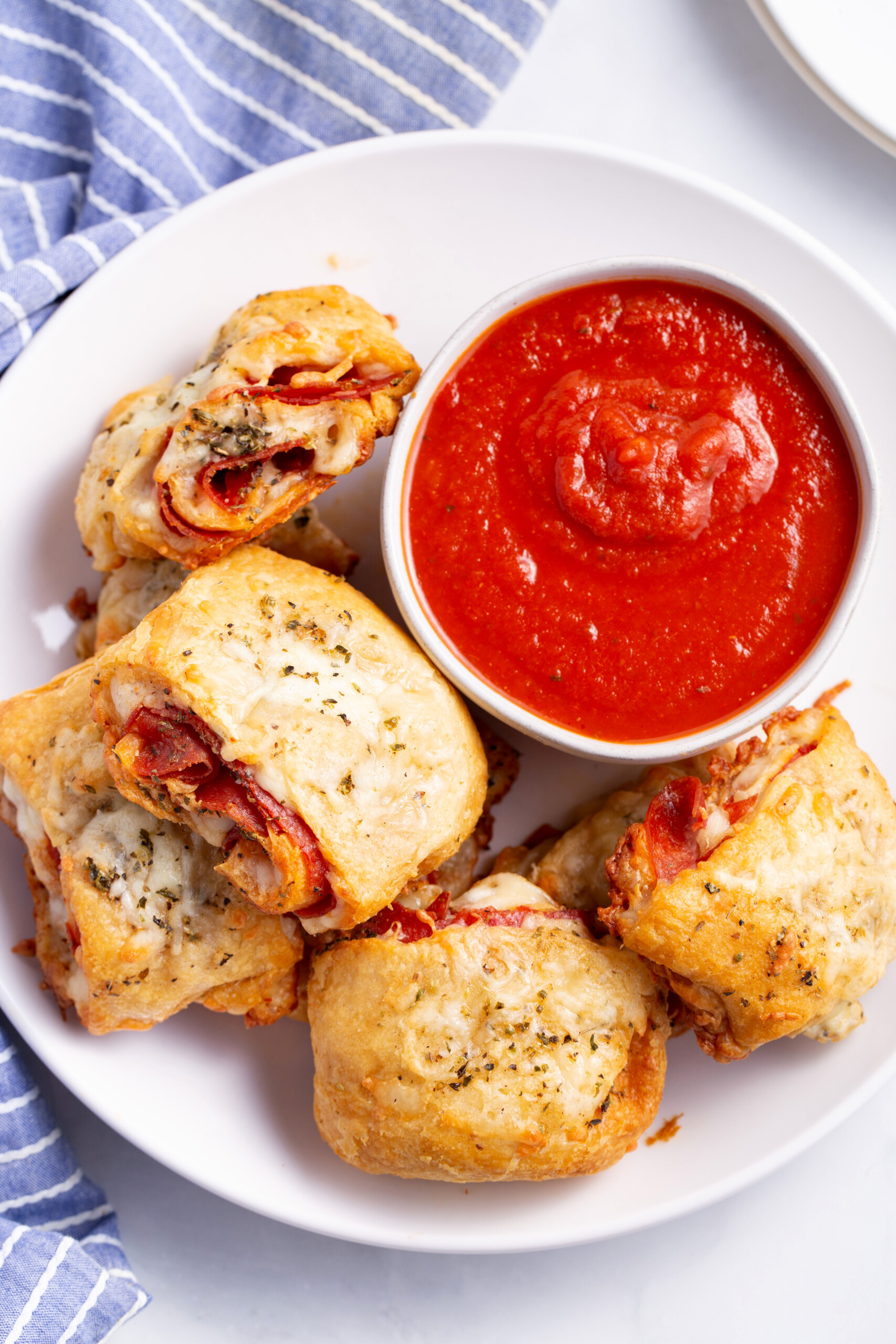 top down image of a plate of pepperoni rollups with a bowl of marinara dipping sauce