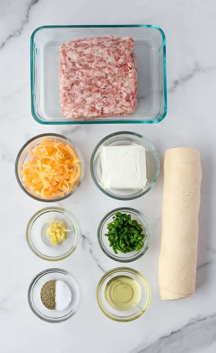 The ingredients to make sausage pinwheels are shown on a white background: oil, salt and pepper, crescent dough, cream cheese, shredded cheese, garlic, chives, and sausage.