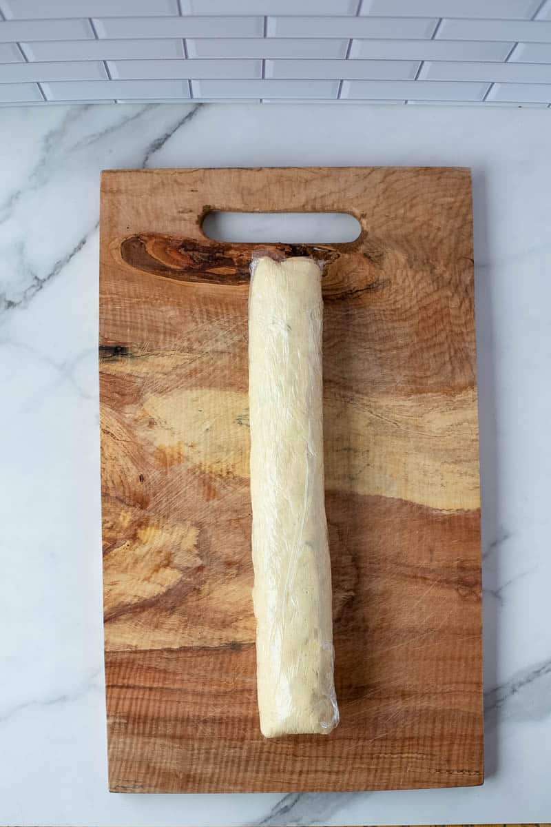 A log of sausage pinwheels is rolled up on a wooden cutting board.