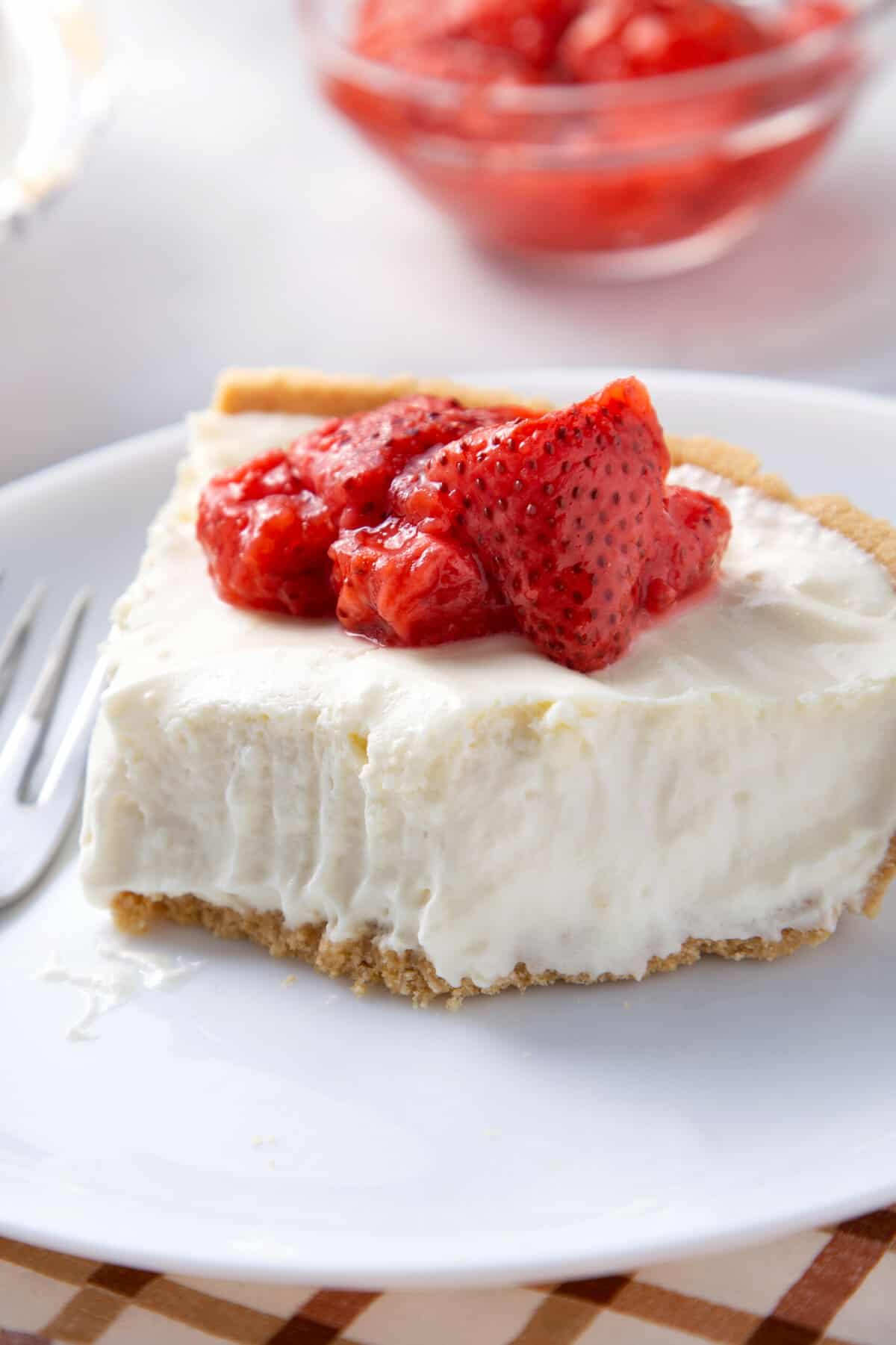 slice of 3-ingredients no-bake cheesecake topped with macerated strawberries served on a white round plate