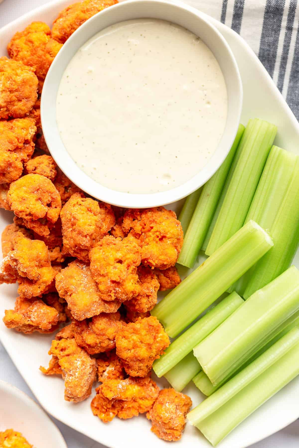 top down image of a plate of air fried buffalo cauliflower, celery sticks and a bowl of ranch served on a large oval white plate