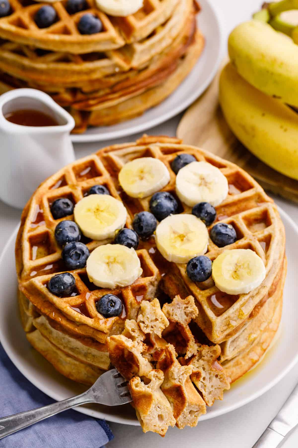 cross section shown of a stack of banana pancakes topped with sliced fresh bananas, blueberries and syrup