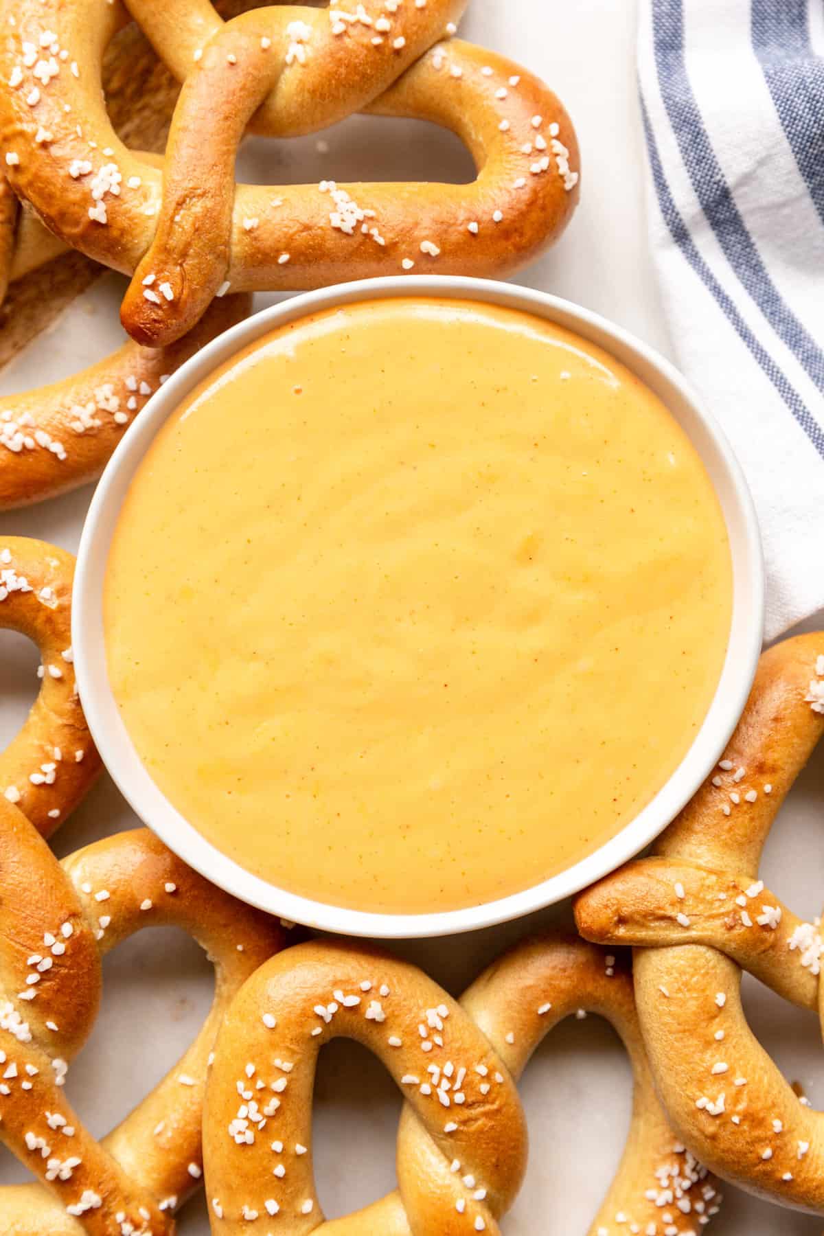top down image and close up of pretzel cheese dip served in a white round bowl surrounded by salted soft pretzels