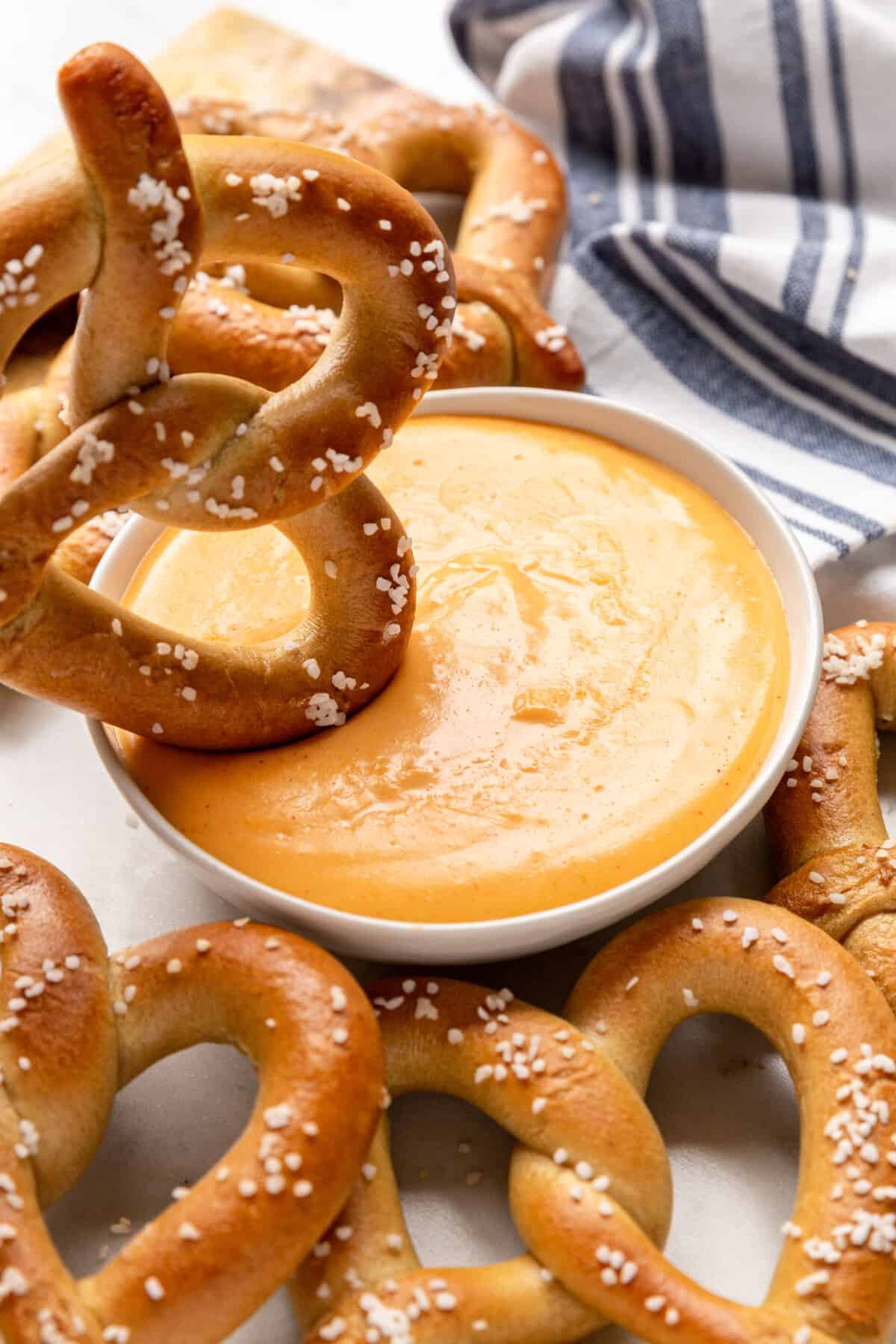 A large soft pretzel being dipped into a bowl of cheese dip.