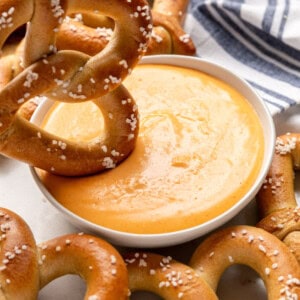 A large soft pretzel being dipped into a bowl of cheese dip.