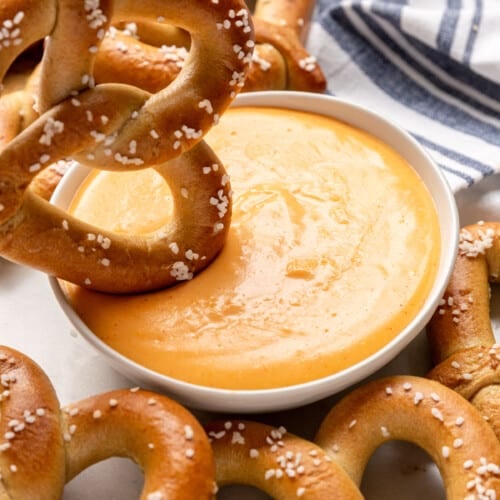 A large soft pretzel being dipped into a bowl of cheese dip.