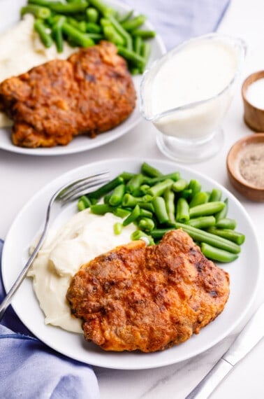 Two plates of air fryer chicken fried steak with mashed potatoes and green beans.