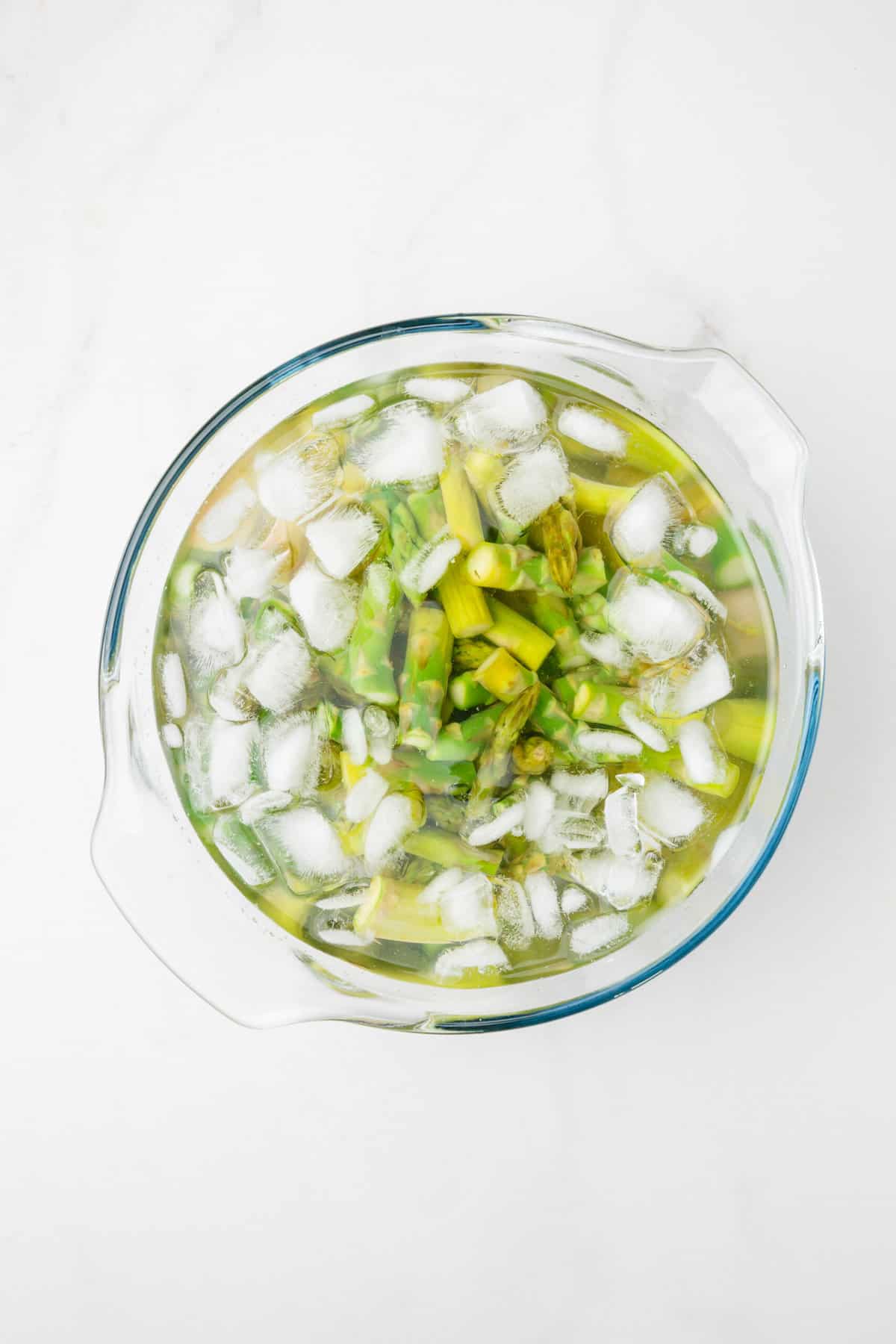 cut and cooked asparagus sitting in an ice bath in a large glass bowl. 