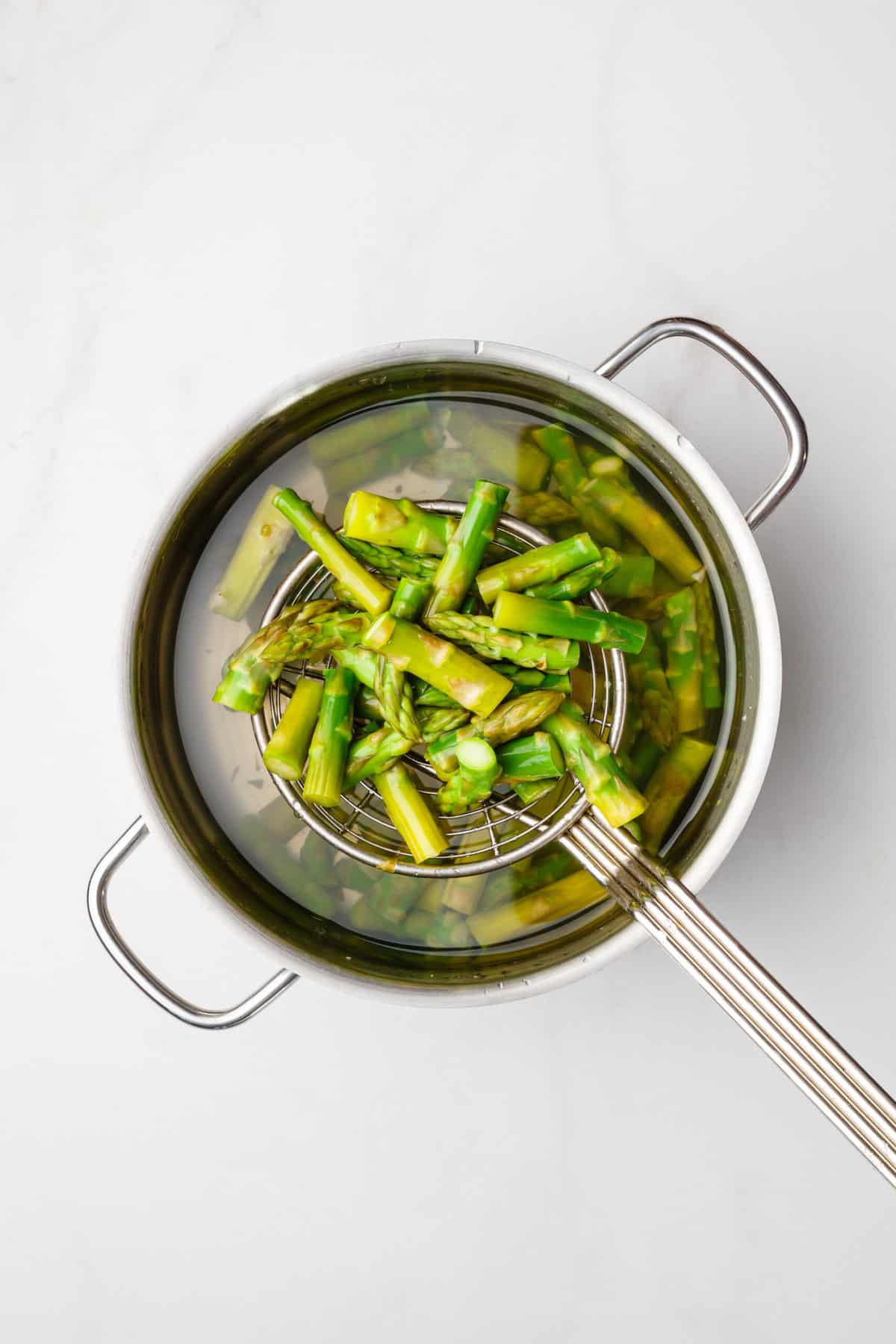 asparagus blanched in a cooking pot and being pulled out using a handheld colander.