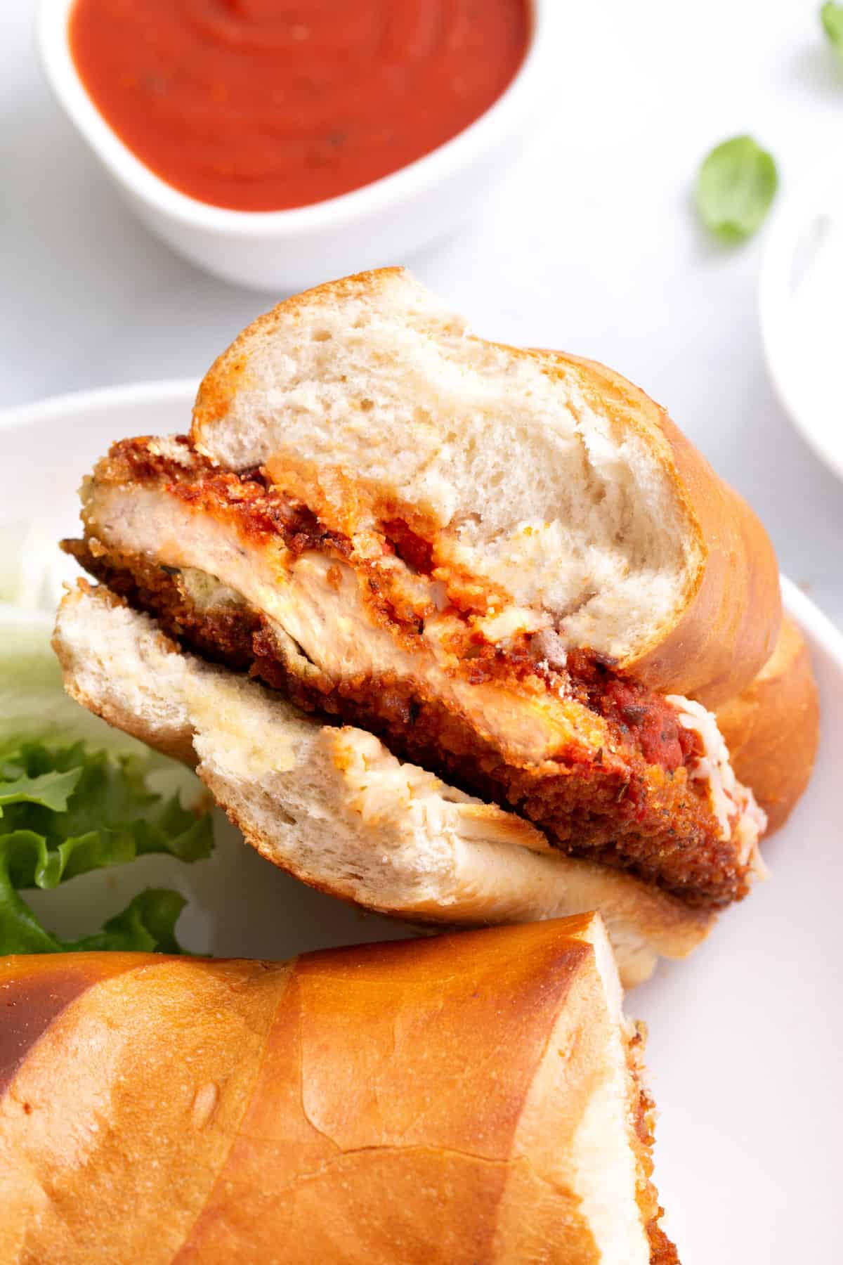 close up image of the cross section of a chicken parmesan sandwich served on a white round plate