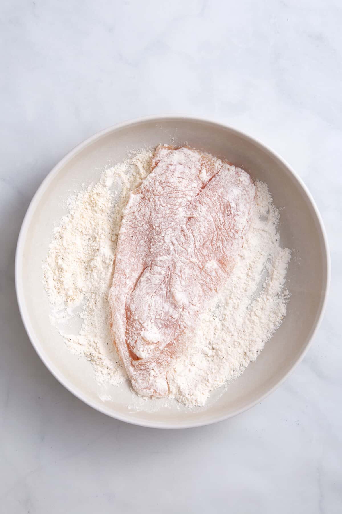 step 1 to make chicken parmesan sandwiches, chicken in a plate of flour.