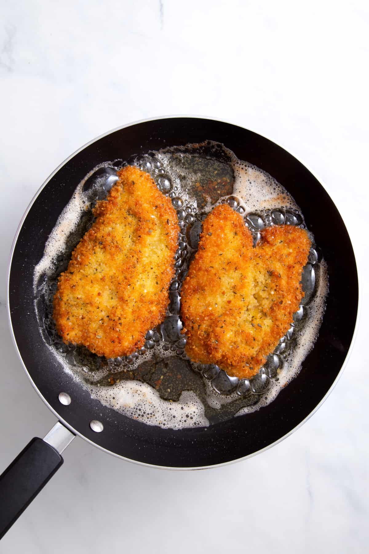 step 4 to make chicken parmesan sandwiches, chicken frying in a pan.