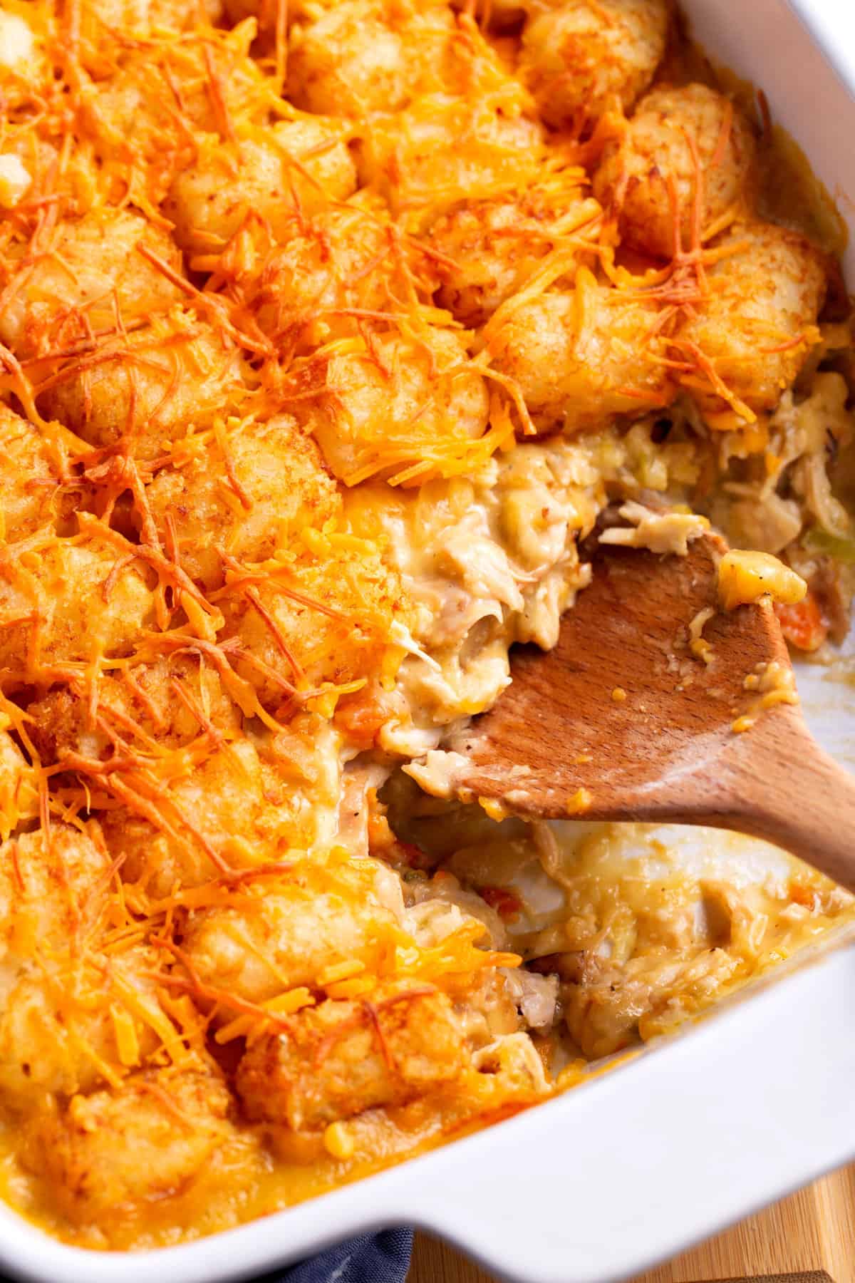 close up image of chicken tater tot casserole with a wooden spoon digging in.