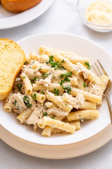 A plate of crockpot chicken alfredo with a piece of garlic bread on the side.