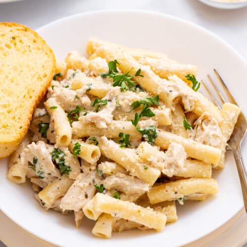 A plate of crockpot chicken alfredo with a piece of garlic bread on the side.