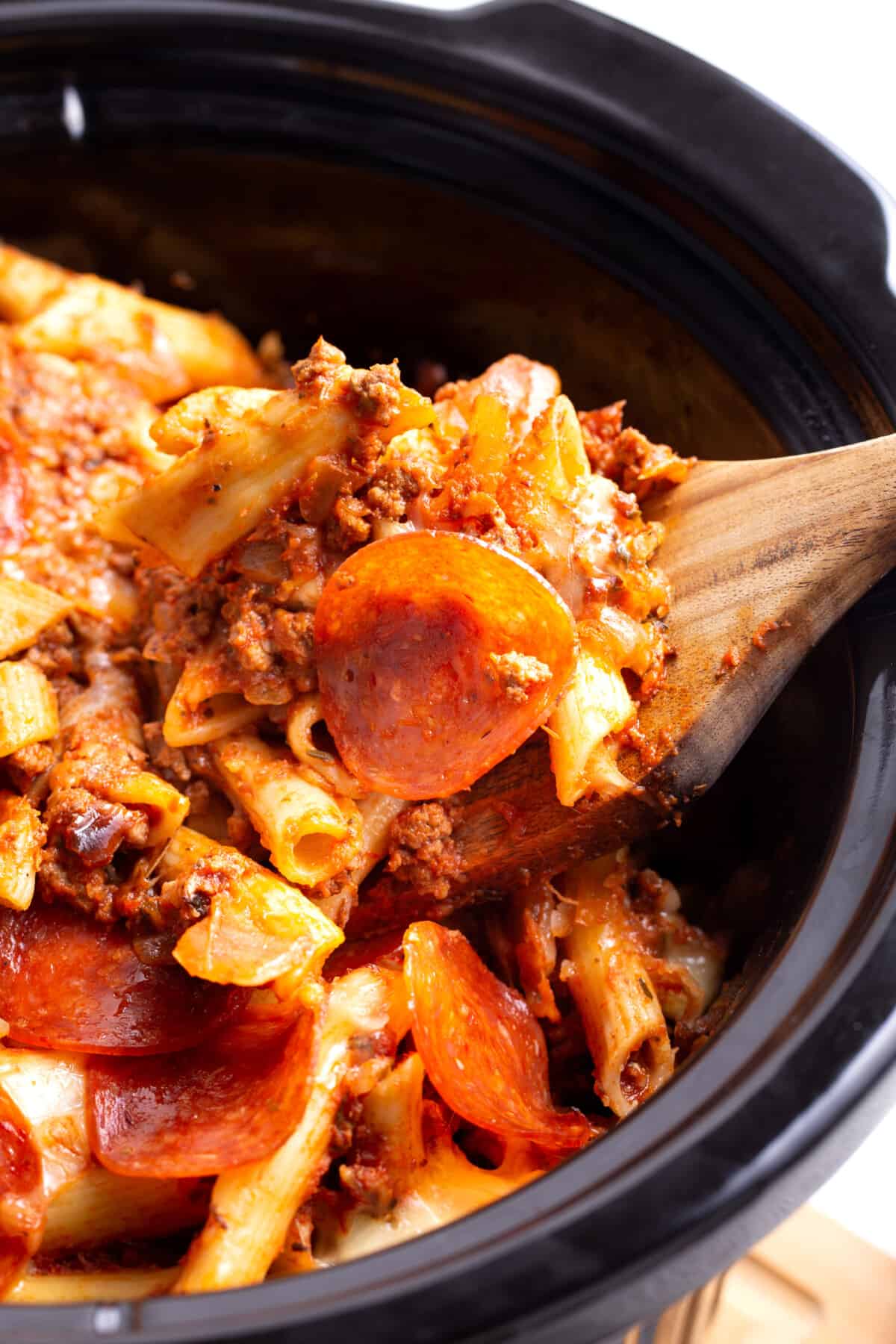 A wooden spoon lifting a scoop of pizza casserole from a crockpot.
