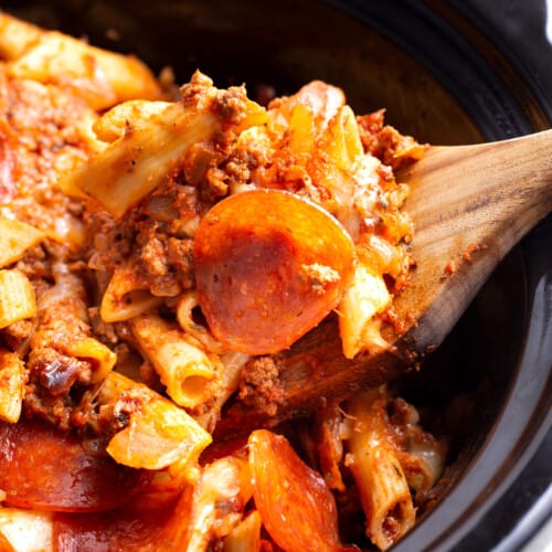 A wooden spoon lifting a scoop of pizza casserole from a crockpot.