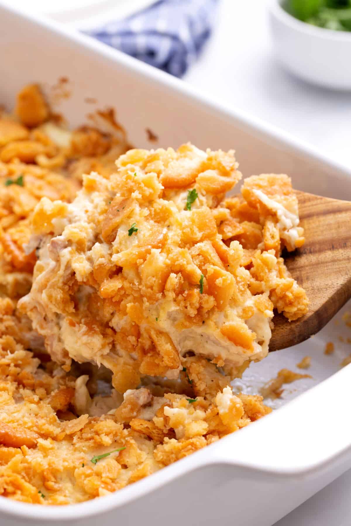 A wooden spoon scoops million dollar chicken casserole from a baking dish.