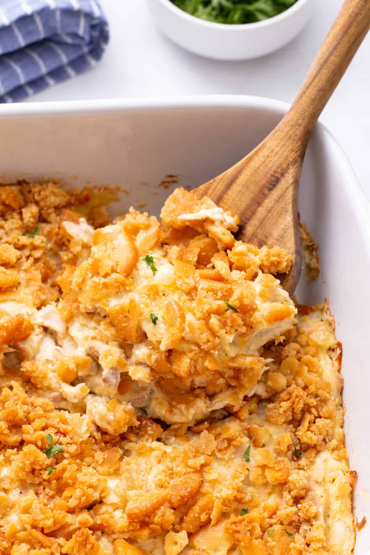 A wooden spoon lifting a serving of million dollar chicken casserole from a baking dish.